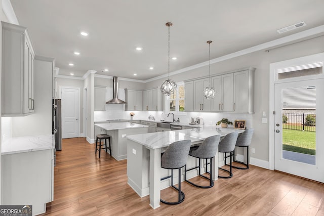 kitchen with appliances with stainless steel finishes, a breakfast bar area, plenty of natural light, wall chimney exhaust hood, and visible vents