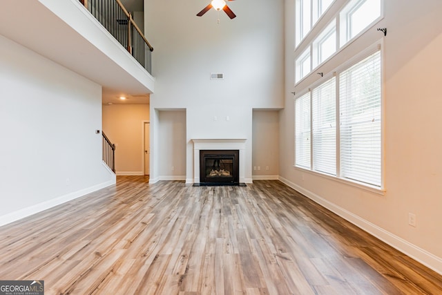 unfurnished living room featuring ceiling fan, wood finished floors, stairway, baseboards, and a towering ceiling
