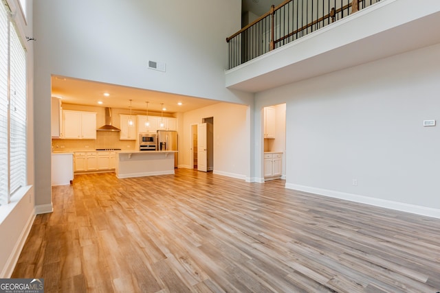 unfurnished living room with a towering ceiling, baseboards, and light wood-style floors