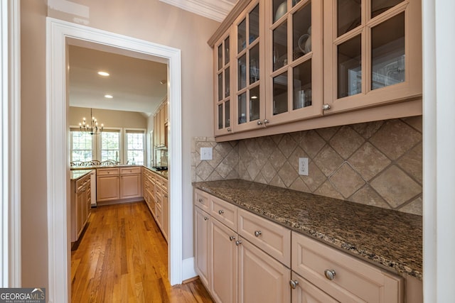 kitchen with backsplash, glass insert cabinets, dark stone countertops, light wood-style floors, and an inviting chandelier