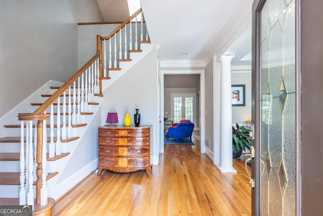 foyer featuring light wood-type flooring, ornamental molding, stairway, and ornate columns