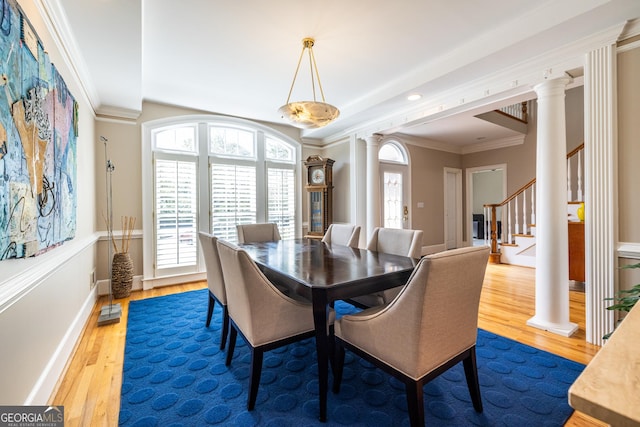 dining room featuring stairs, ornate columns, ornamental molding, baseboards, and wood finished floors