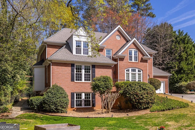 view of front facade with a shingled roof, french doors, a front yard, and brick siding