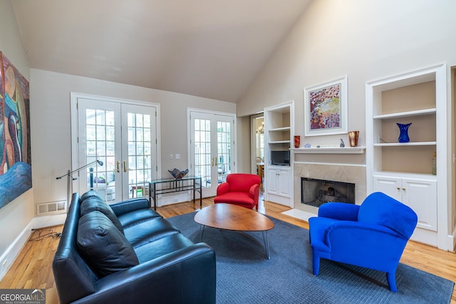 living area with french doors, light wood-style flooring, a high end fireplace, and visible vents