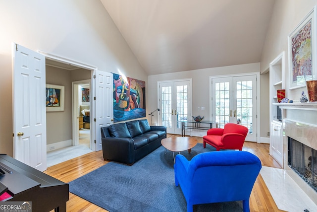 living area with light wood-type flooring, french doors, high vaulted ceiling, baseboards, and a fireplace