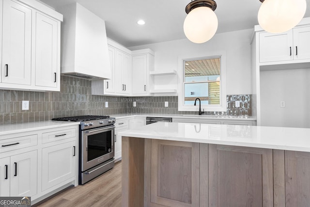 kitchen with stainless steel gas range oven, a sink, light countertops, open shelves, and premium range hood