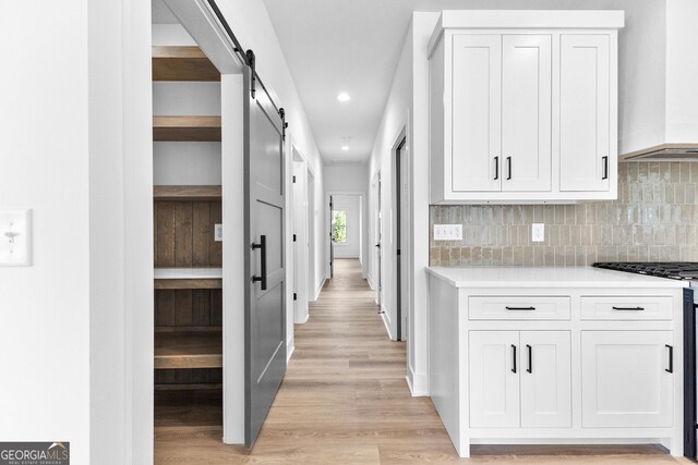 corridor featuring light wood finished floors, a barn door, and recessed lighting