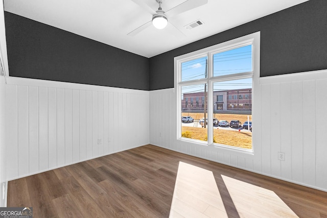 empty room with wood finished floors, wainscoting, and a ceiling fan