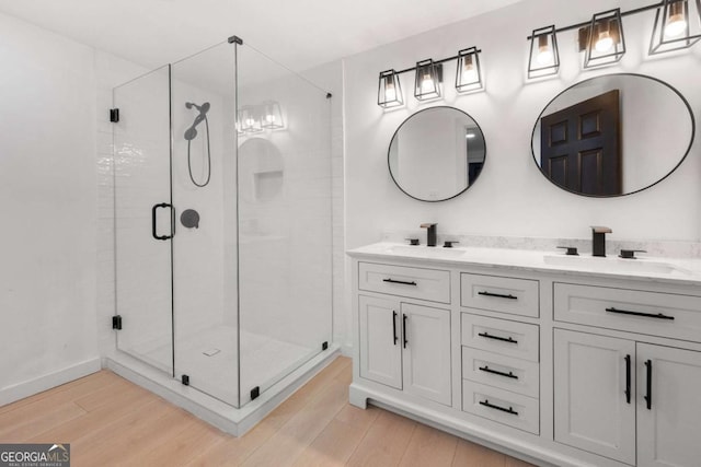 full bath featuring a stall shower, double vanity, wood finished floors, and a sink