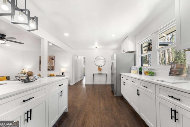 kitchen with light stone counters, freestanding refrigerator, white cabinetry, ceiling fan, and dark wood-type flooring
