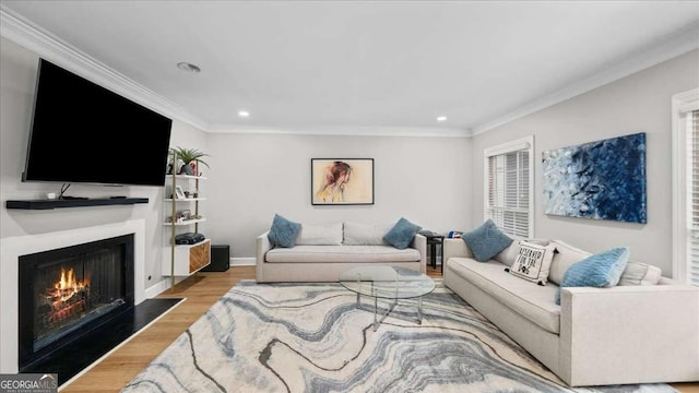 living room featuring a lit fireplace, light wood-style flooring, recessed lighting, and crown molding