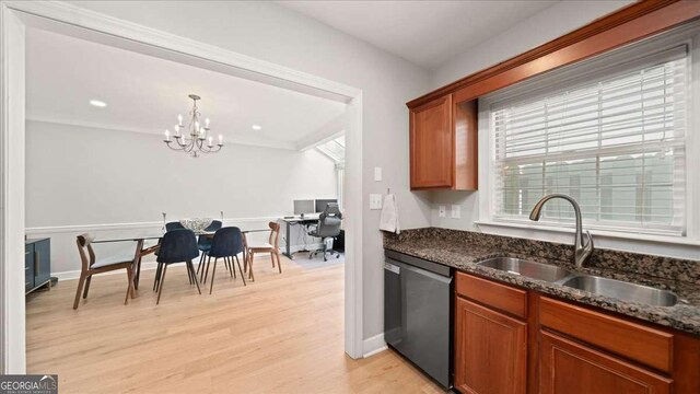 kitchen featuring light wood finished floors, dark stone countertops, a sink, dishwashing machine, and a notable chandelier