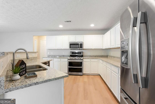 1924 Sweet Flag Rd, Lawrenceville, GA 30045 - kitchen with stainless steel appliances, a sink, a textured ceiling, light wood-type flooring, and white cabinetry
