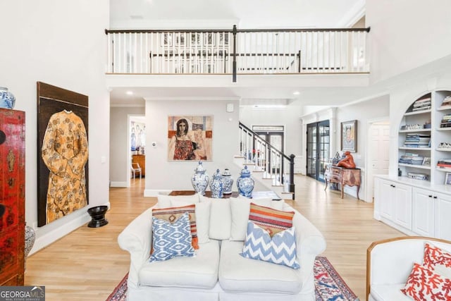 living area with a towering ceiling, baseboards, stairs, and light wood-type flooring