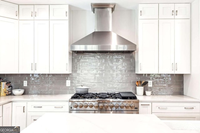 kitchen featuring gas range, wall chimney exhaust hood, decorative backsplash, and white cabinets