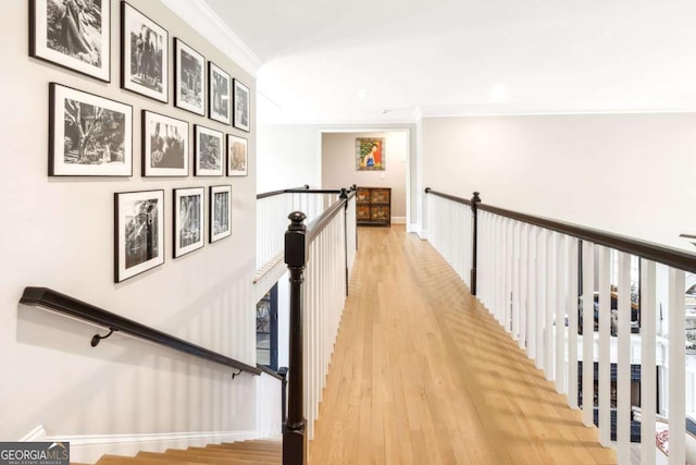hallway featuring baseboards, an upstairs landing, light wood-style flooring, and ornamental molding