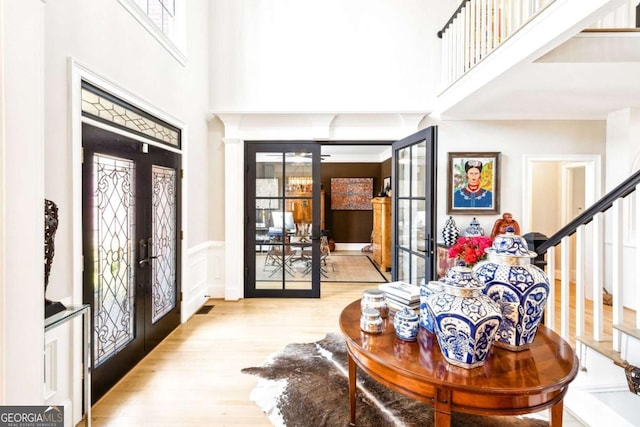 foyer featuring a wainscoted wall, french doors, stairway, a high ceiling, and wood finished floors