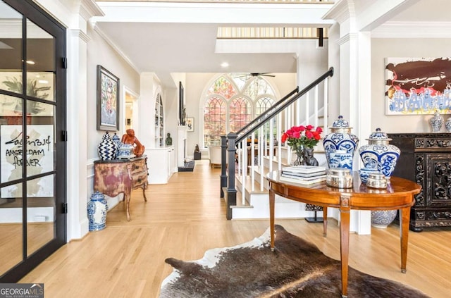 entrance foyer featuring ornate columns, ornamental molding, wood finished floors, and stairway