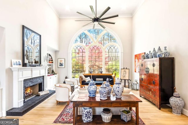 living room with light wood-style flooring, a ceiling fan, crown molding, and a fireplace