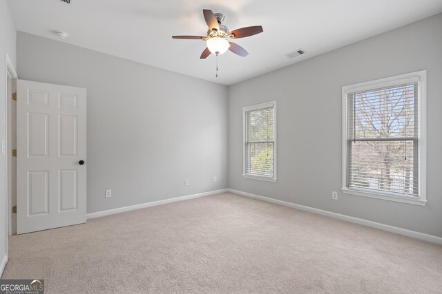empty room with baseboards, visible vents, ceiling fan, and carpet