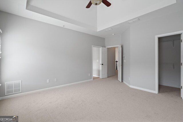 unfurnished bedroom featuring light colored carpet, visible vents, baseboards, and a walk in closet