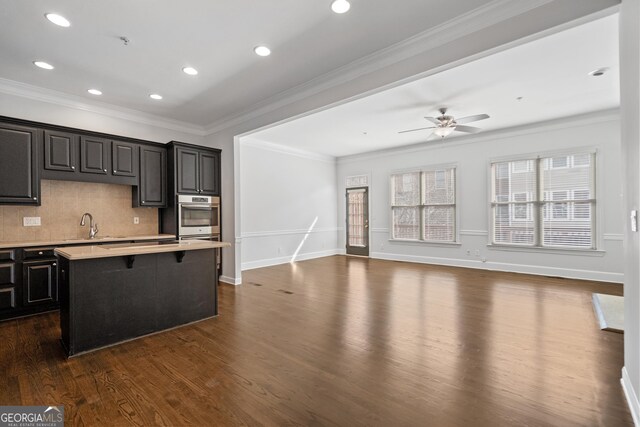 kitchen with dark wood-style flooring, light countertops, oven, a breakfast bar, and a kitchen island