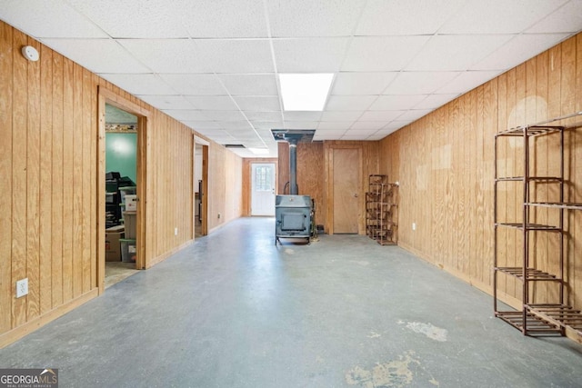 below grade area with a wood stove, a paneled ceiling, and wooden walls