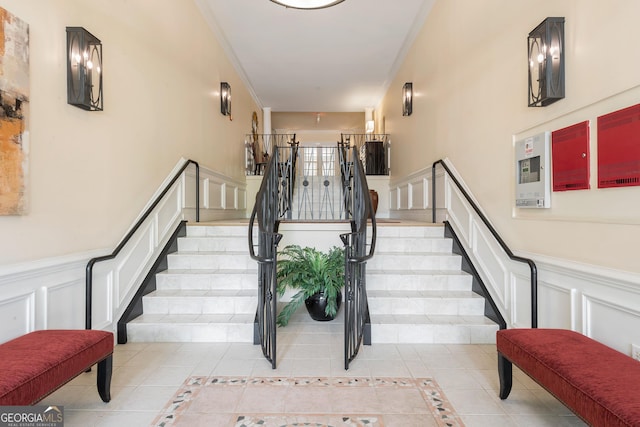stairs with a decorative wall, tile patterned flooring, a wainscoted wall, and crown molding