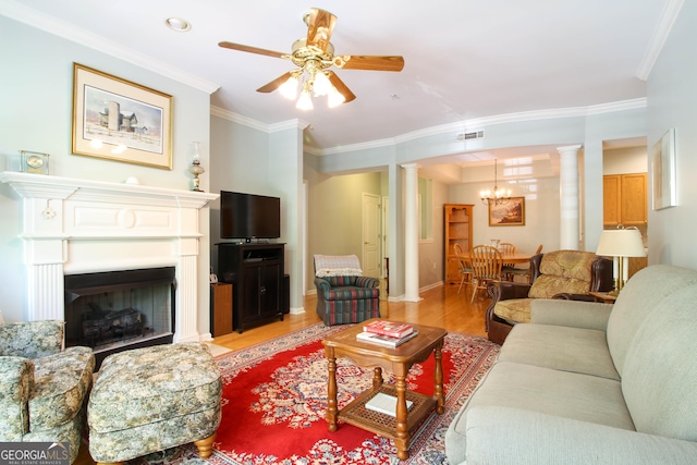 living room featuring ornate columns, ornamental molding, ceiling fan with notable chandelier, light wood finished floors, and a fireplace