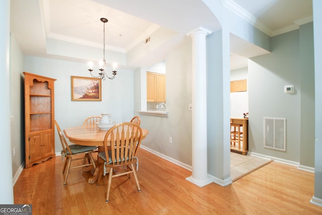 dining area featuring a chandelier, light wood finished floors, a raised ceiling, visible vents, and ornamental molding