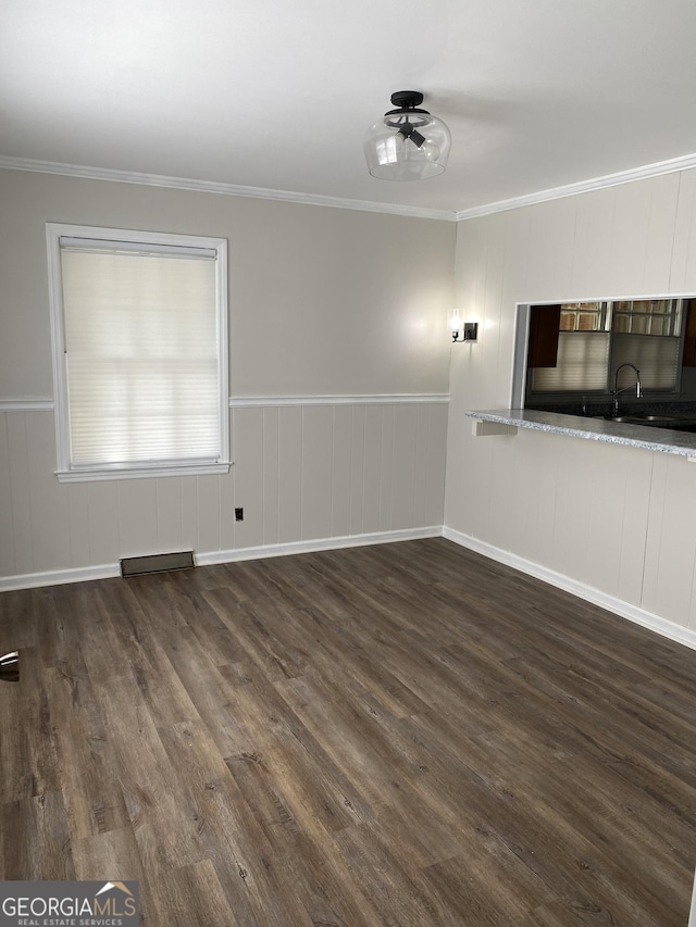 unfurnished living room featuring a wainscoted wall, dark wood finished floors, visible vents, ceiling fan, and ornamental molding
