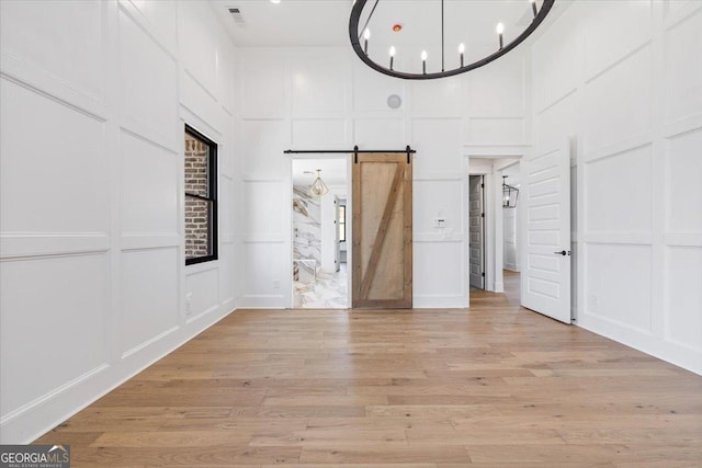 100 Forest Pl, Forsyth, GA 31029 - empty room featuring a decorative wall, a high ceiling, a barn door, light wood-type flooring, and a chandelier