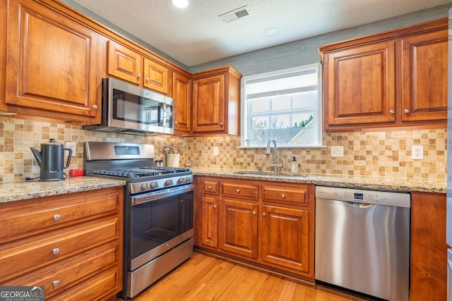 kitchen with a sink, visible vents, brown cabinetry, and appliances with stainless steel finishes