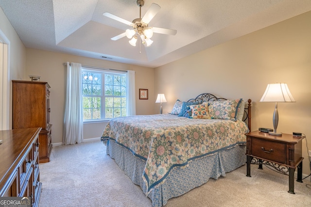 bedroom featuring a textured ceiling, baseboards, ceiling fan, a tray ceiling, and light colored carpet