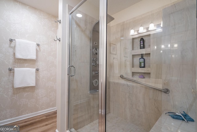 full bathroom featuring wood finished floors, wallpapered walls, baseboards, and a shower stall