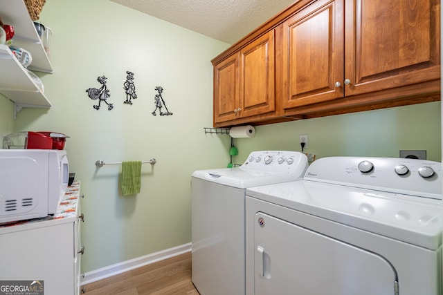 clothes washing area featuring a textured ceiling, baseboards, washer and dryer, light wood-style floors, and cabinet space