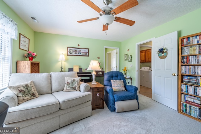 living area with light colored carpet, a textured ceiling, independent washer and dryer, visible vents, and ceiling fan