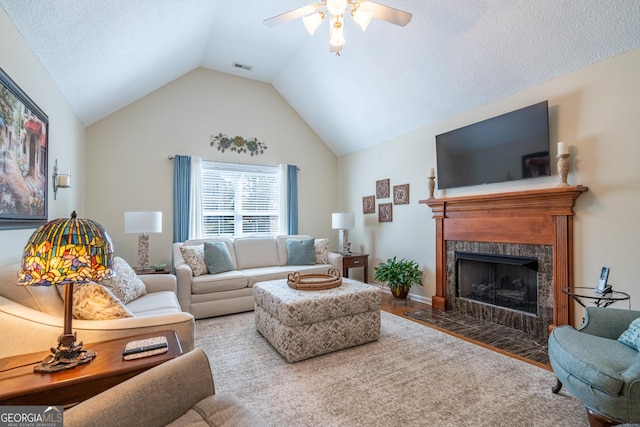 living room with visible vents, wood finished floors, a tiled fireplace, a ceiling fan, and vaulted ceiling
