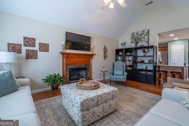 living room with visible vents, baseboards, a fireplace, wood finished floors, and a ceiling fan