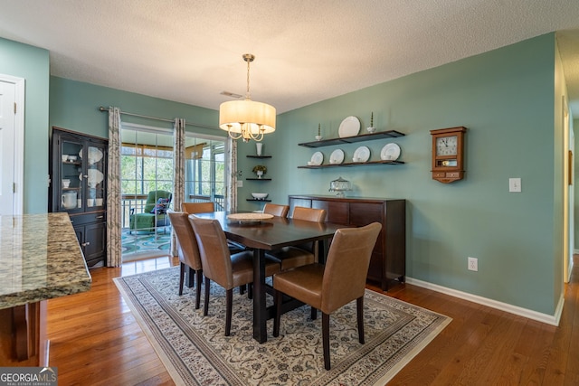 dining area featuring hardwood / wood-style floors, a notable chandelier, baseboards, and a textured ceiling