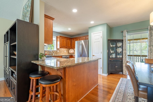 kitchen with light stone counters, tasteful backsplash, appliances with stainless steel finishes, a peninsula, and light wood-type flooring