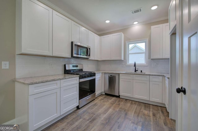 kitchen with wood finished floors, stainless steel appliances, white cabinets, a sink, and visible vents