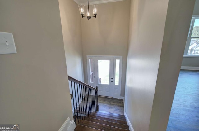 entrance foyer with crown molding, baseboards, an inviting chandelier, wood-type flooring, and stairs