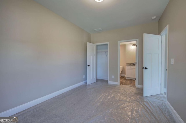 unfurnished bedroom featuring a closet, a spacious closet, light carpet, baseboards, and ensuite bathroom