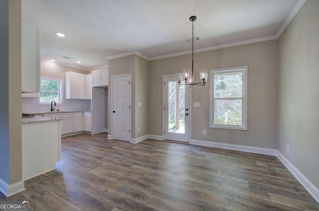 unfurnished dining area with ornamental molding, a notable chandelier, dark wood finished floors, and baseboards