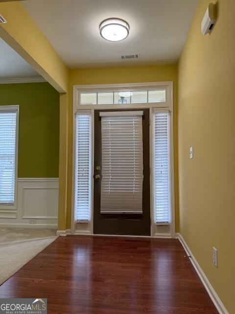 foyer featuring a wainscoted wall, a decorative wall, visible vents, crown molding, and wood finished floors