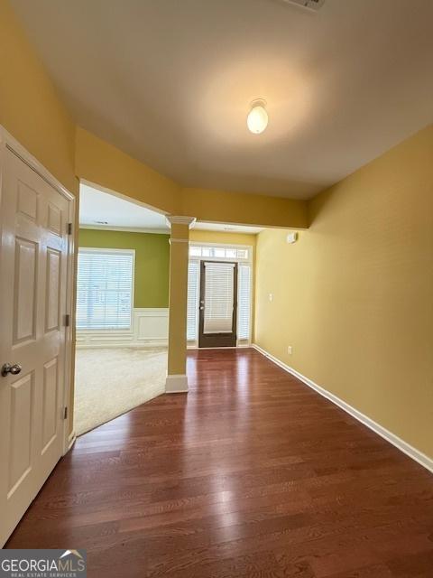 interior space with dark wood-type flooring, decorative columns, and wainscoting