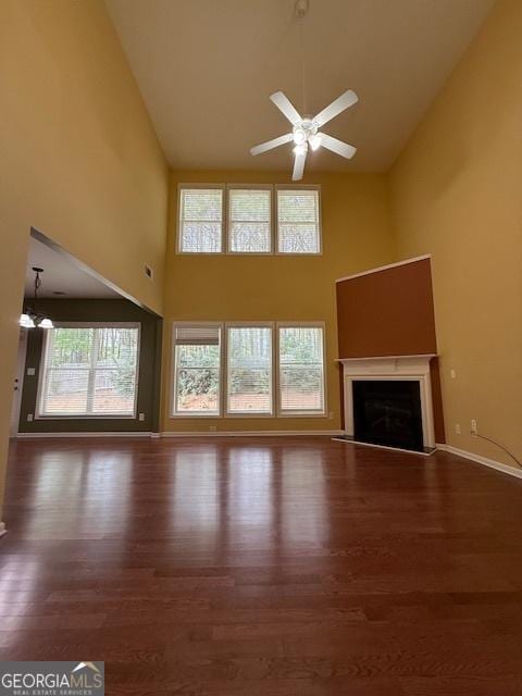 unfurnished living room with high vaulted ceiling, wood finished floors, a glass covered fireplace, baseboards, and ceiling fan