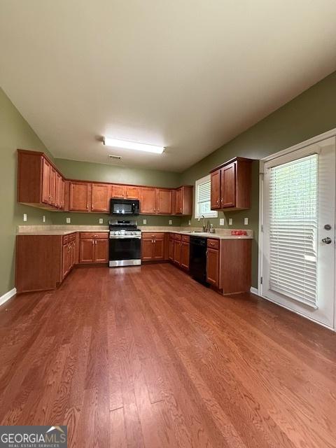 kitchen featuring light countertops, plenty of natural light, dark wood-type flooring, black appliances, and brown cabinetry
