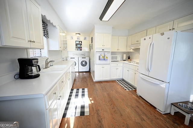 kitchen featuring washer and clothes dryer, a sink, wood finished floors, under cabinet range hood, and white appliances